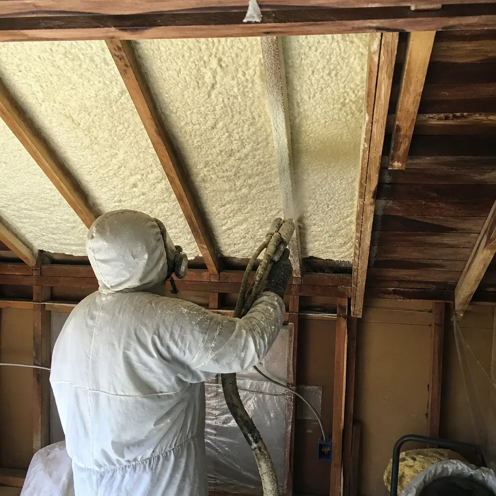 Contractor applying professional spray foam insulation to attic rafters